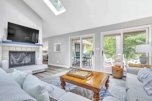 A modern living room with a fireplace, a flat-screen TV, and a large window overlooking a patio area.