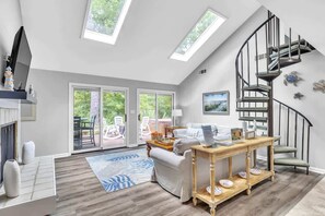 Ein großzügiger Wohnraum mit hohen Decken, Oberlichtern, Holzboden, einer Couch, einem Couchtisch, einer Wendeltreppe und Blick durch große Glastüren.