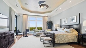 A spacious bedroom with a large bed, a desk, and a chair, a window with curtains, and a ceiling fan. - Seasonal, Monthly, Annual (Marco Island)