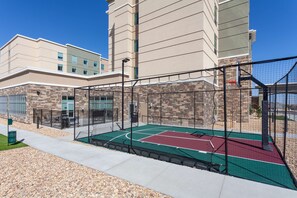 An outdoor basketball court with a net, surrounded by a fence, and a building with a stone facade in the background. - Homewood Suites by Hilton Broomfield Boulder (Broomfield)