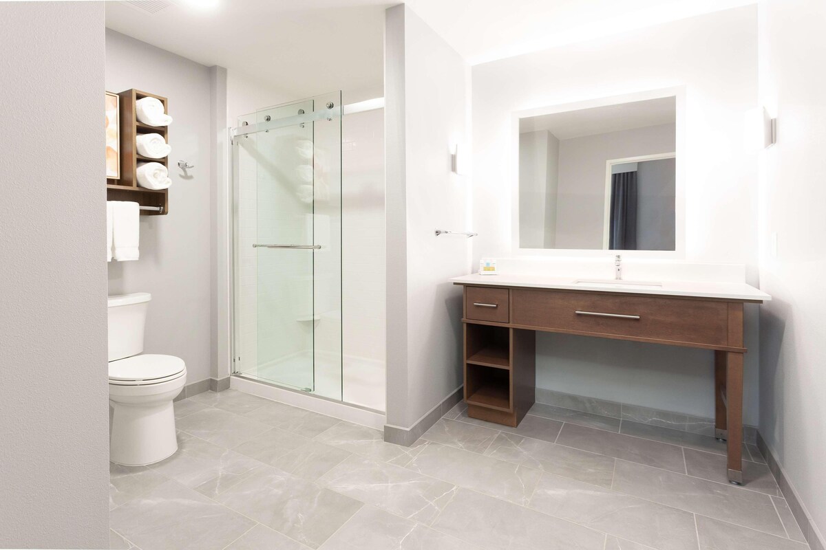 A modern bathroom with a glass-enclosed shower, a white toilet, a wooden vanity with a mirror, and a towel rack with neatly folded towels.