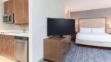 Habitación de hotel con cama, televisión de pantalla plana, cómoda de madera, microondas y lavavajillas.
