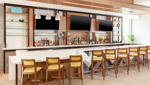 A modern bar area with a long counter, multiple bar stools, and shelves stocked with bottles. - Homewood Suites by Hilton Broomfield Boulder (Broomfield)