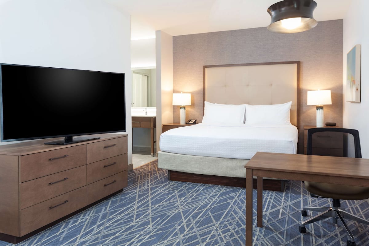 A hotel room with a bed, a desk, a television, and a bathroom visible in the background.