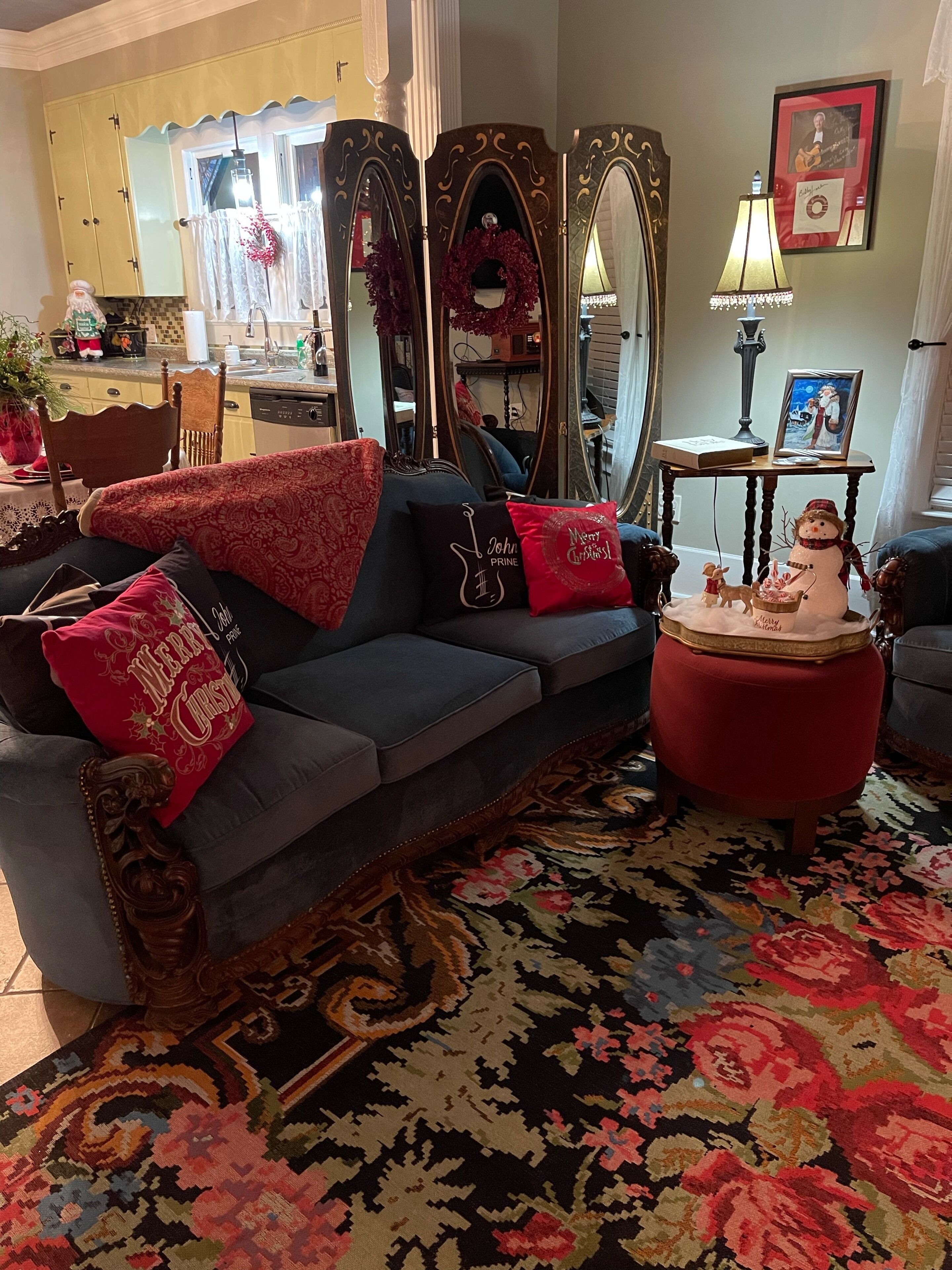 A cozy living room with a dark grey sofa, red and gold cushions, a red ottoman, and a decorative snowman.