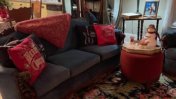 A cozy living room with a dark grey sofa, red and gold cushions, a red ottoman, and a decorative snowman.