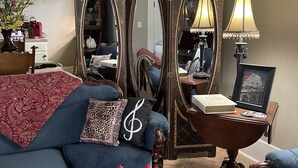 Un salon avec un canapé bleu, un miroir décoratif, une lampe et un vase contenant des tulipes rouges.