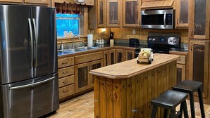 A kitchen with wooden cabinets, a stainless steel refrigerator, a microwave, and a sink.