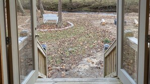 An open door leading to a backyard with a wooden deck, a metal bench, and a fish mounted on the wall.