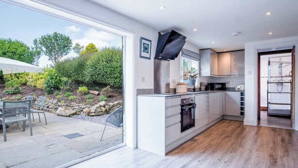 Een moderne keuken met witte kastjes, een ingebouwde oven en een groot raam met uitzicht op een tuin.