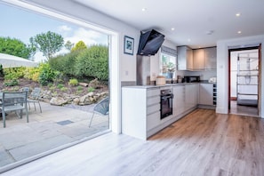 A modern kitchen with white cabinets, a built-in oven, and a large window overlooking a garden.