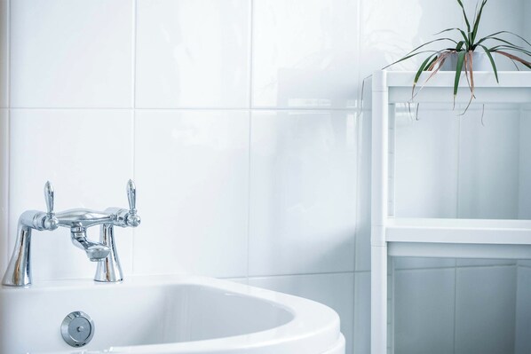 A white bathroom with a chrome faucet, a white sink, and a potted plant on a shelf.