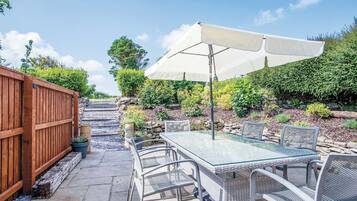 An outdoor patio with a glass-top table and metal chairs, an umbrella, and a wooden fence.