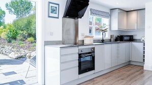 Een moderne keuken met een inbouwoven, een magnetron en een groot raam met uitzicht op een tuin.