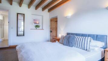 A bedroom with a large bed, wooden beams on the ceiling, a bedside table with a lamp, and a mirror on the wall.