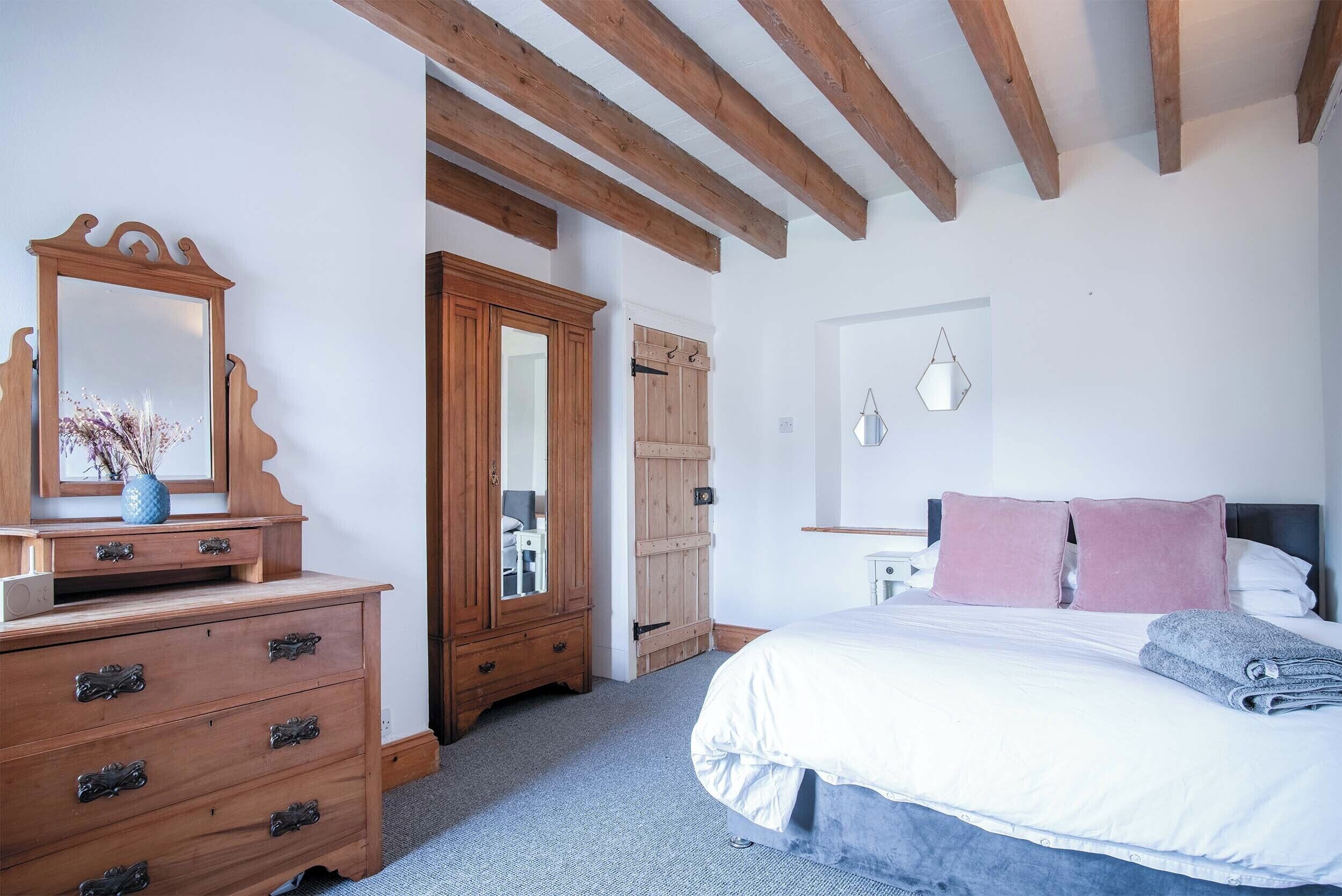 A bedroom with a wooden dresser, a bed with white bedding, and a wooden wardrobe.