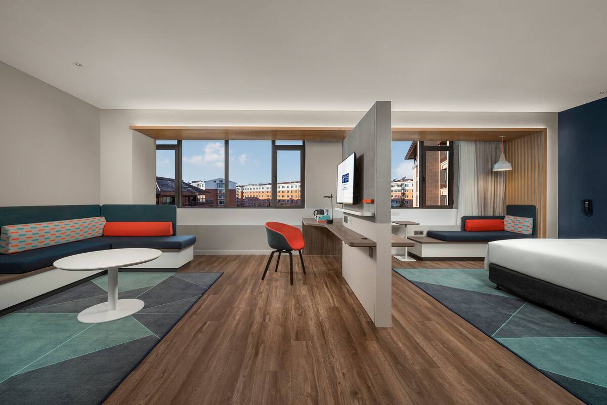Une chambre d’hôtel moderne avec un canapé, un lit, un bureau et une vue sur la ville.