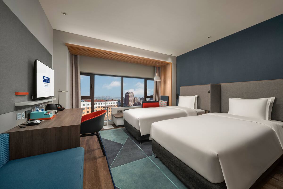 Une chambre d’hôtel moderne avec deux lits, un bureau, une chaise et une vue sur la ville.
