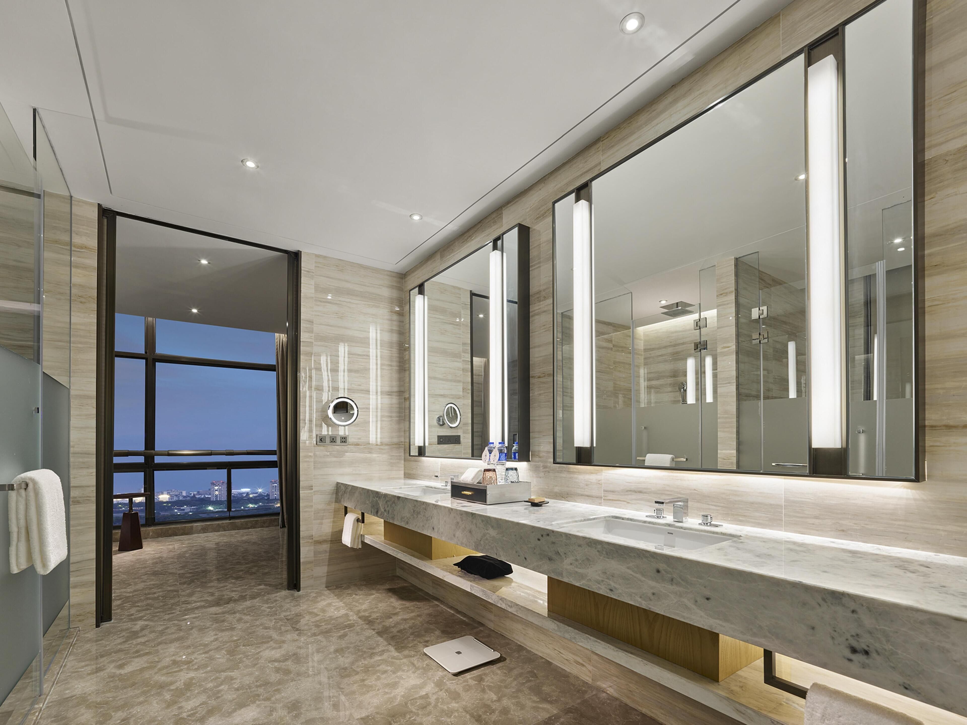 Un baño moderno con un espejo grande, un tocador con lavamanos y vistas a la ciudad.