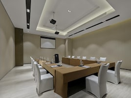 Un salón de conferencias con una larga mesa, sillas, un proyector y una pantalla.