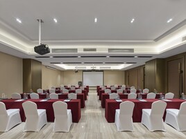 Un salón de conferencias con mesas, sillas y una pantalla para proyector.