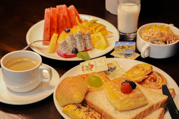 Un plato de desayuno con croissants, tostadas, fruta y una taza de café.