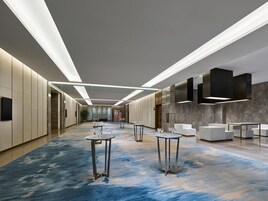 Un moderno vestíbulo de hotel con un largo pasillo, varias zonas de estar y un mostrador de recepción.