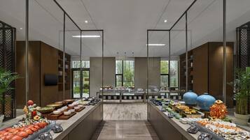 Montaje de bufé con mariscos y diversos platos, interior moderno con divisiones de vidrio y vistas a zonas verdes.