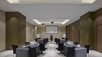 Une salle de conférence dotée d’un écran de projection central, de plusieurs tables avec des chaises et d’un plafond équipé d’un éclairage encastré.