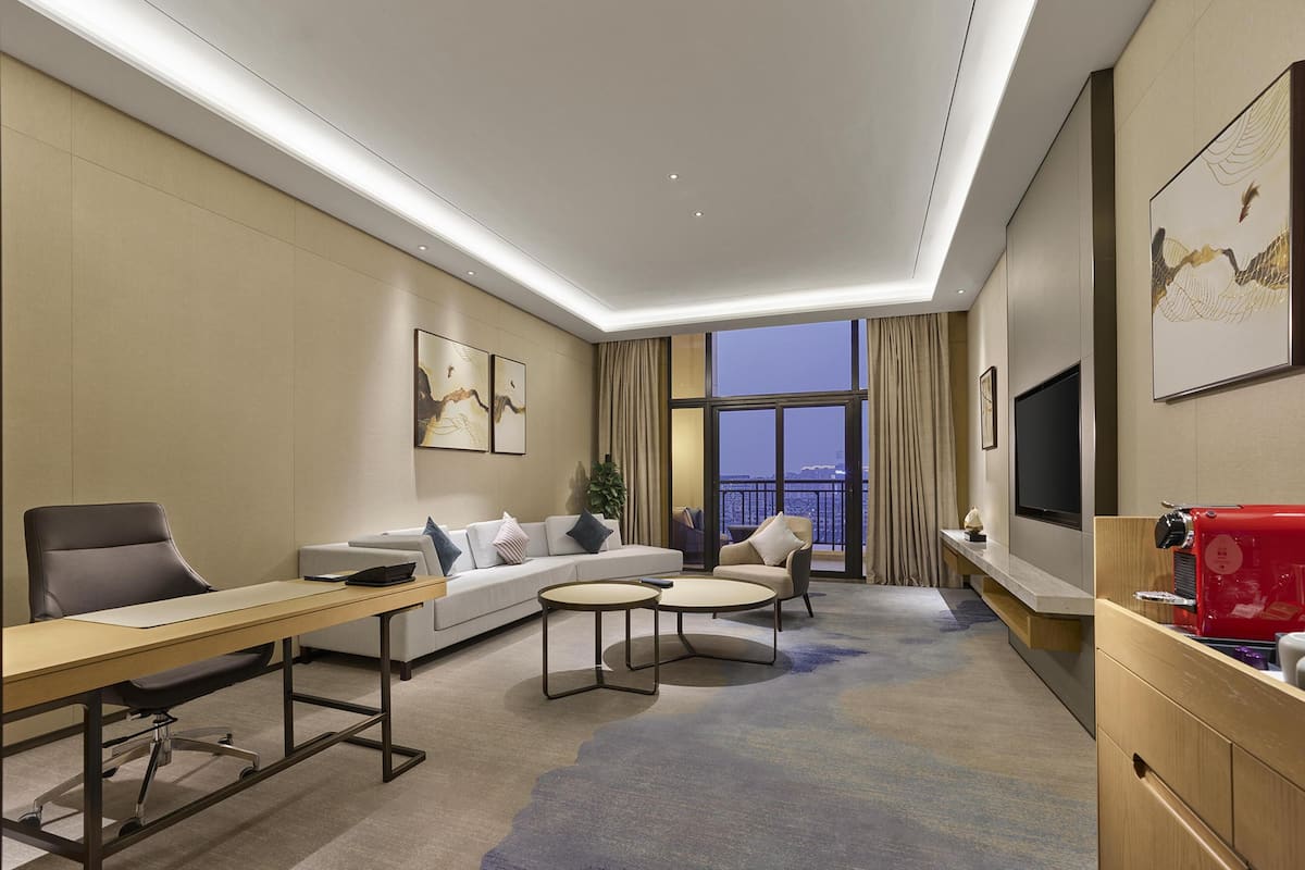 Ein modernes Hotelzimmer mit einer Couch, einem Schreibtisch, einer Kaffeemaschine und einem Fernseher.