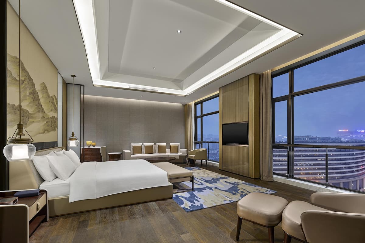 Ein modernes Hotelzimmer mit großem Bett, Sitzgelegenheit, Fernseher und Blick auf die Stadt.