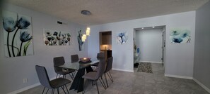 A dining area with a glass table and chairs, surrounded by walls with floral artwork. - ❤ Beautiful Oceanfront Condo (Hollywood)