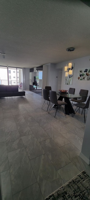 Uma sala de estar ampla com sofá, mesa de jantar e cadeiras, e uma janela grande.