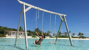 Eine Person schwingt über klarem türkisblauem Wasser, im Hintergrund ein Strand und Hotelgebäude.