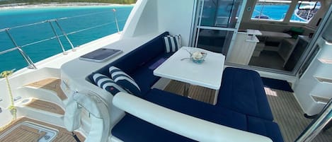Cubierta de barco con zona de estar, una mesita y vista al mar.
