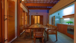 Una mesa de comedor de madera con sillas, una zona de cocina con armarios y un refrigerador, y un techo con vigas de madera y un tragaluz.