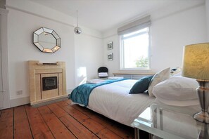 A bedroom with a bed, a mirror, a fireplace, a window, and a lamp. - Sleeps 12 - Themed Accommodation (The City of Brighton and Hove)