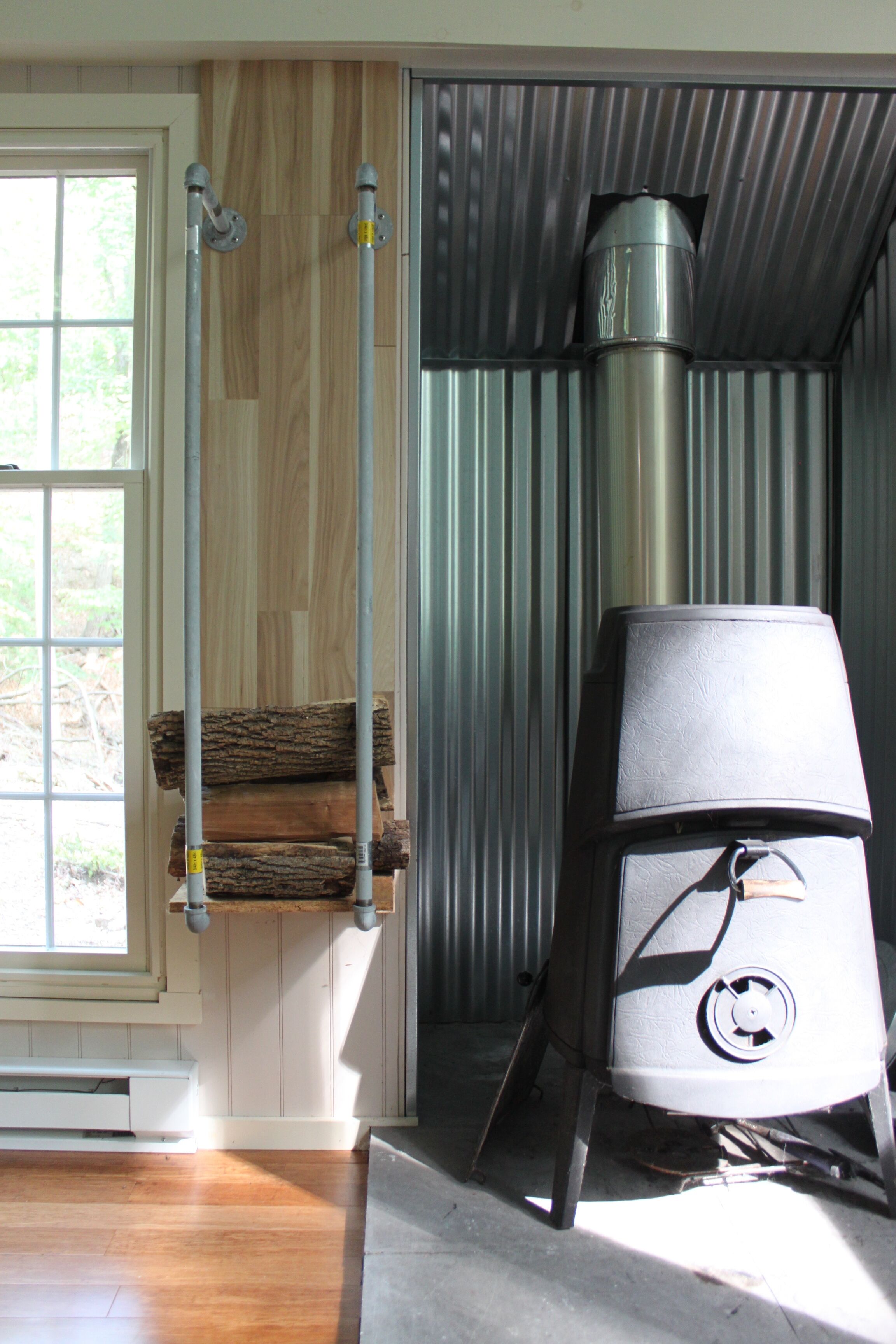 A wood stove in a room with wooden walls and a window.