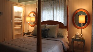 Una camera da letto con un letto, due lampade da comodino, un comodino con una scatola di fazzoletti, uno specchio e un armadio con lo sportello socchiuso.