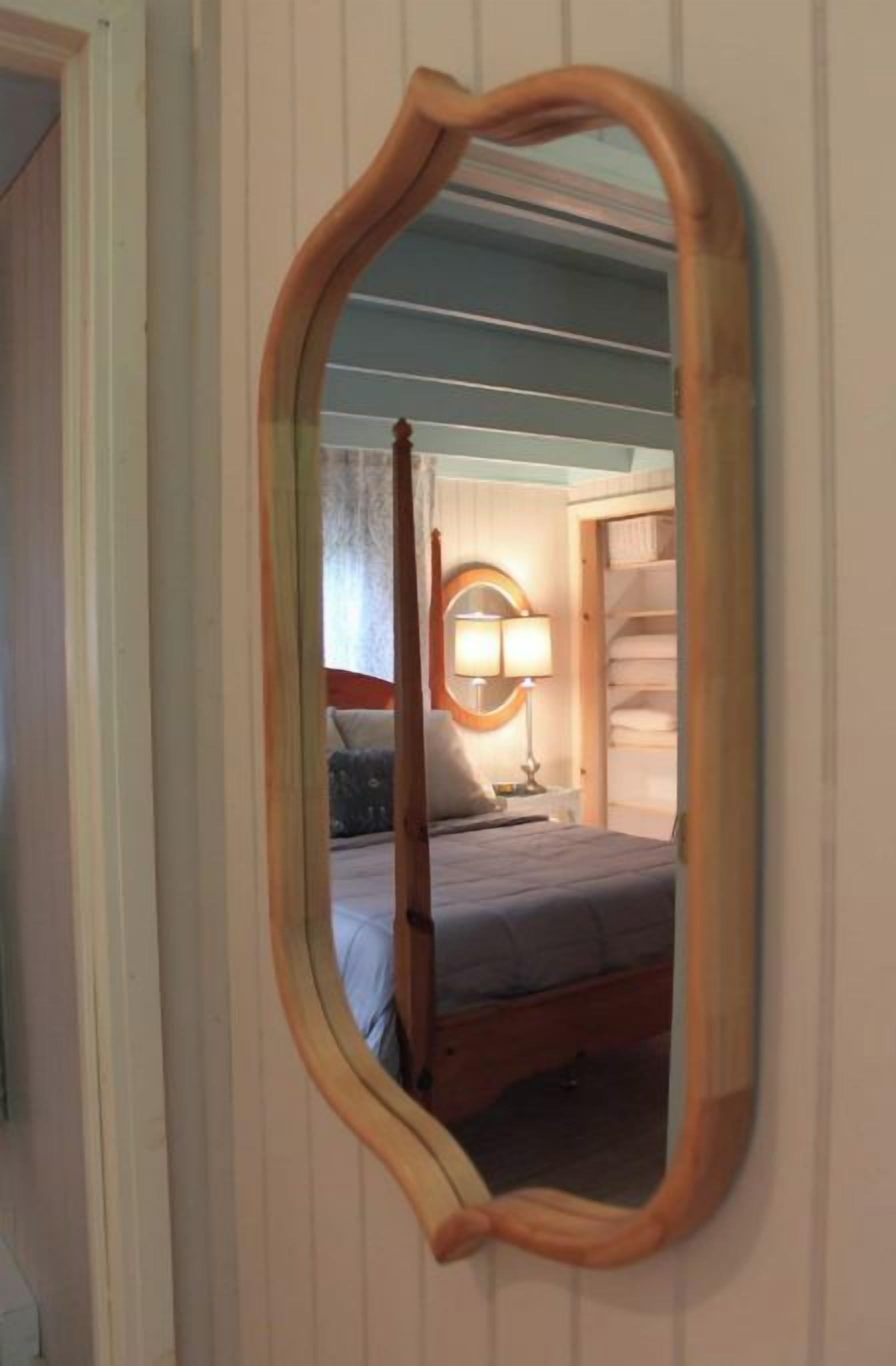 Ein Schlafzimmer mit einem hölzernen Bett, einer Nachttischlampe und einem Spiegel mit Holzrahmen.