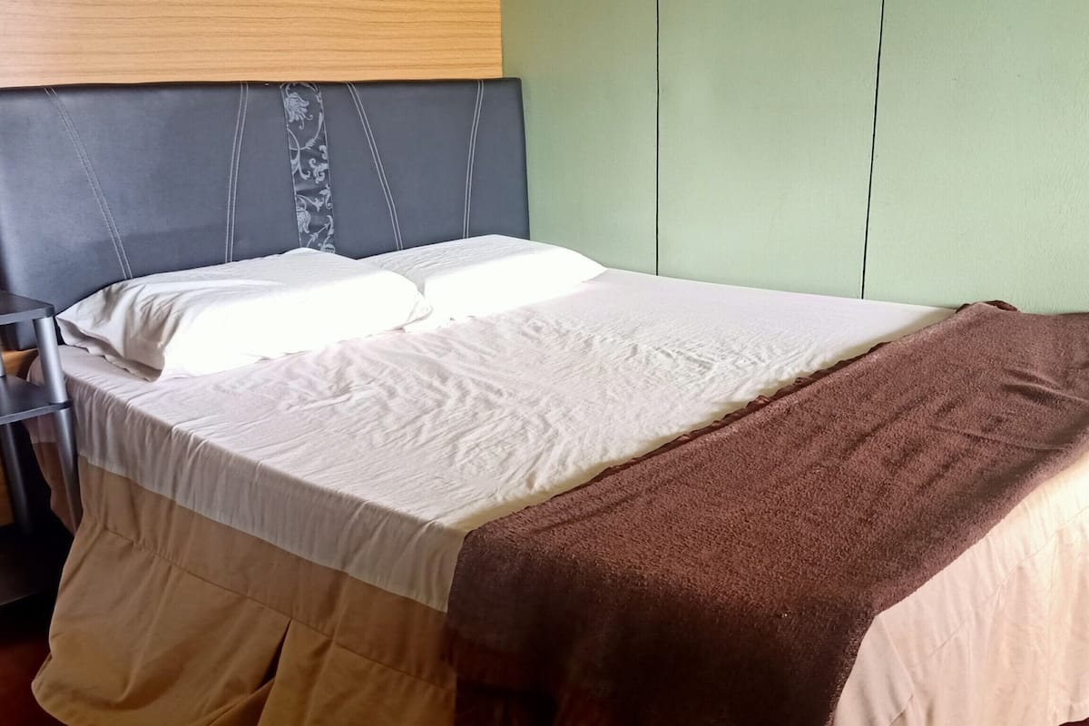Un lit avec une couvre-lit blanche et marron, une tête de lit et un mur vert.