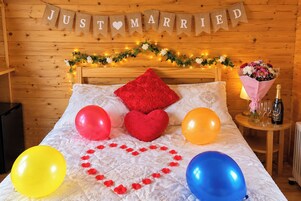 Quarto com cama, um buquê de flores, uma garrafa de champanhe e um letreiro com a mensagem 'APENAS CASADOS'.