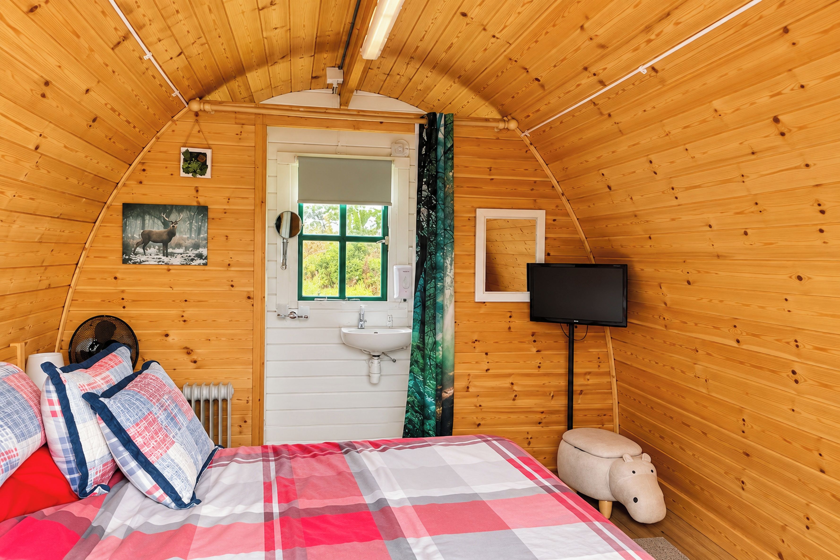 A cozy cabin bedroom with a bed, a bedside table, a mirror, a window with a view, a television, and a radiator.