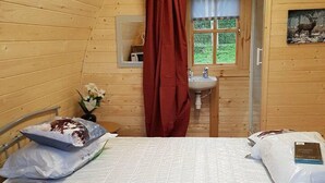 Una camera in una casetta di legno con un letto, una piccola finestra, un lavandino e uno specchio.