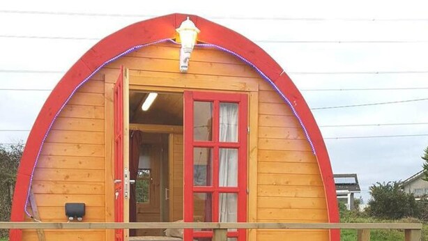 Una baita di legno con un arco rosso, un pontile in legno e un'unica finestra con tende.