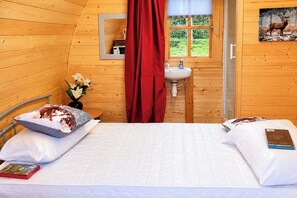 A cozy cabin room with a bed, a window with a view of greenery, a sink, and a mirror. - Glamping Pod in St Austell, Sleeps 2 With Spa Pool (St Austell)