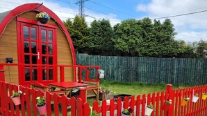 Una struttura in legno rossa con tetto rosso, un portico e un'area recintata con vasi di piante.