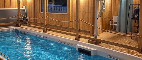 A swimming pool with wooden deck and railings, surrounded by wooden walls and a window with a view.