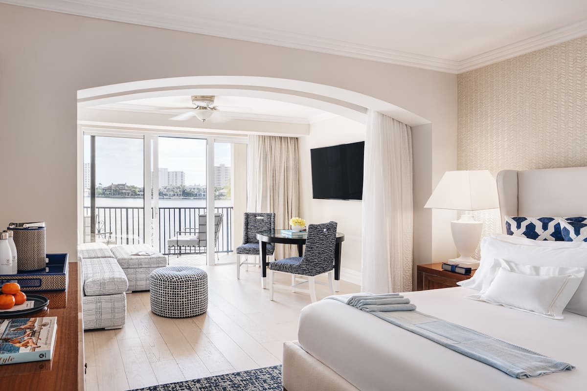 Une chambre d’hôtel dotée d’un grand lit, d’un bureau avec des chaises, d’un balcon offrant une vue agréable et d’un coin repas avec une table et des chaises.