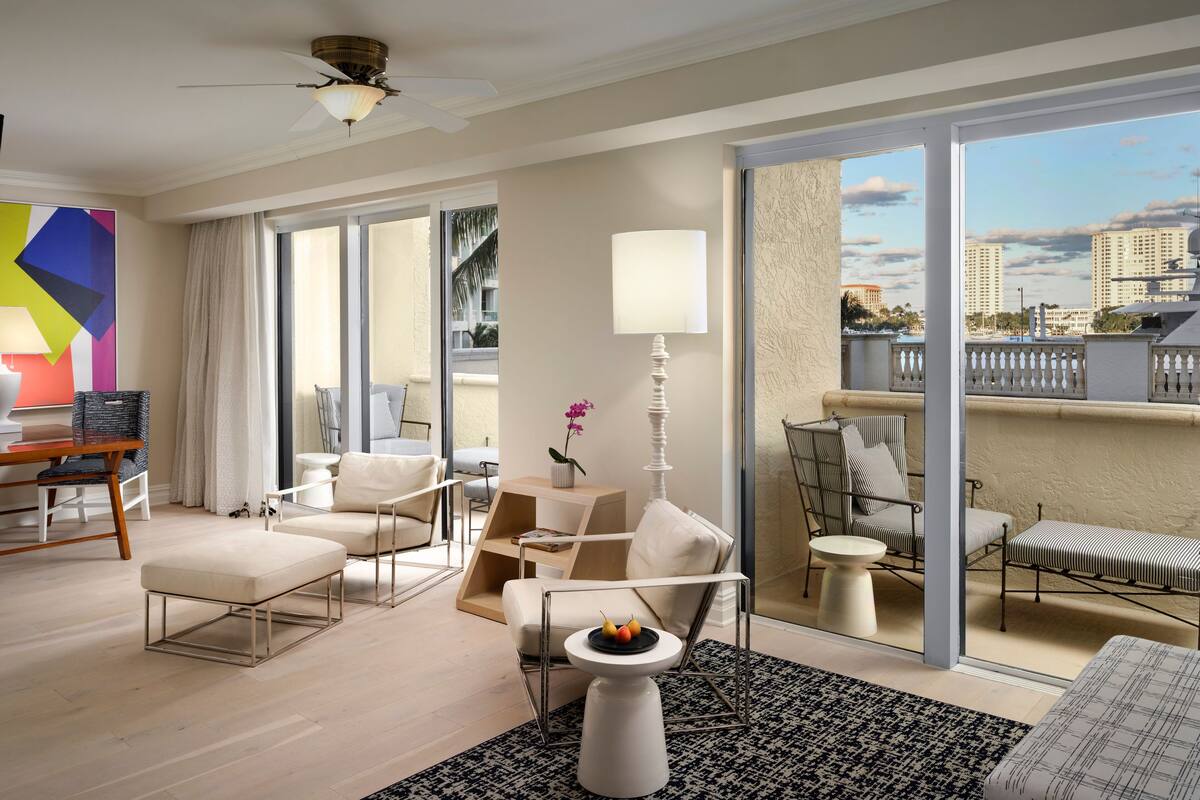 Une chambre d’hôtel moderne dotée d’un balcon, de grandes fenêtres, d’un ventilateur de plafond et offrant une vue sur le paysage urbain.